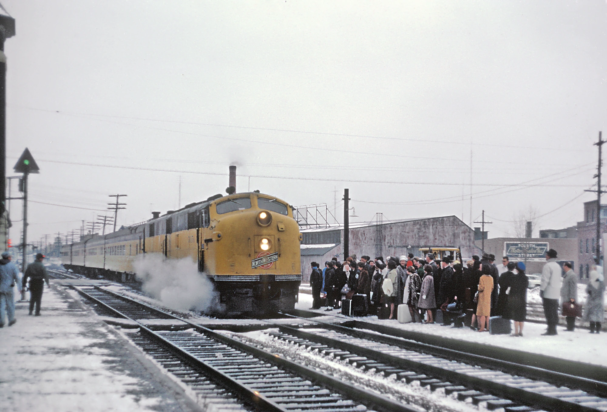 Passengers waiting for a yellow train in snowy winter, rendered in low resolution with dark, light, and yellow dots.